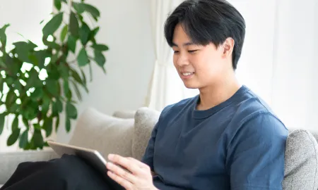 A man smiling while using a tablet on a sofa participating in an online event.