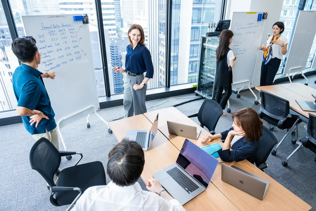 Business school students collaborating in a modern classroom, discussing Financial Ratio Analysis at whiteboards.