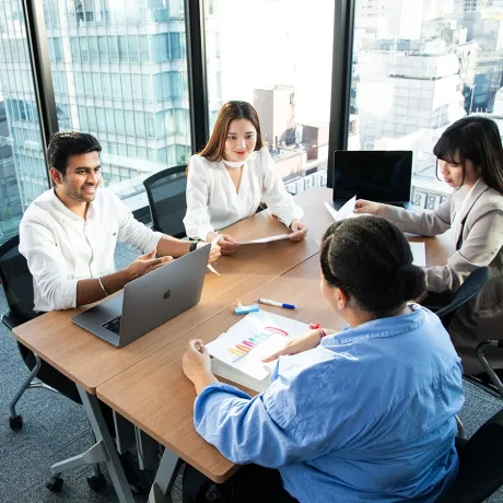 Four diverse students sit around a table in a high-rise office, discussing an assignment during a breakout session.